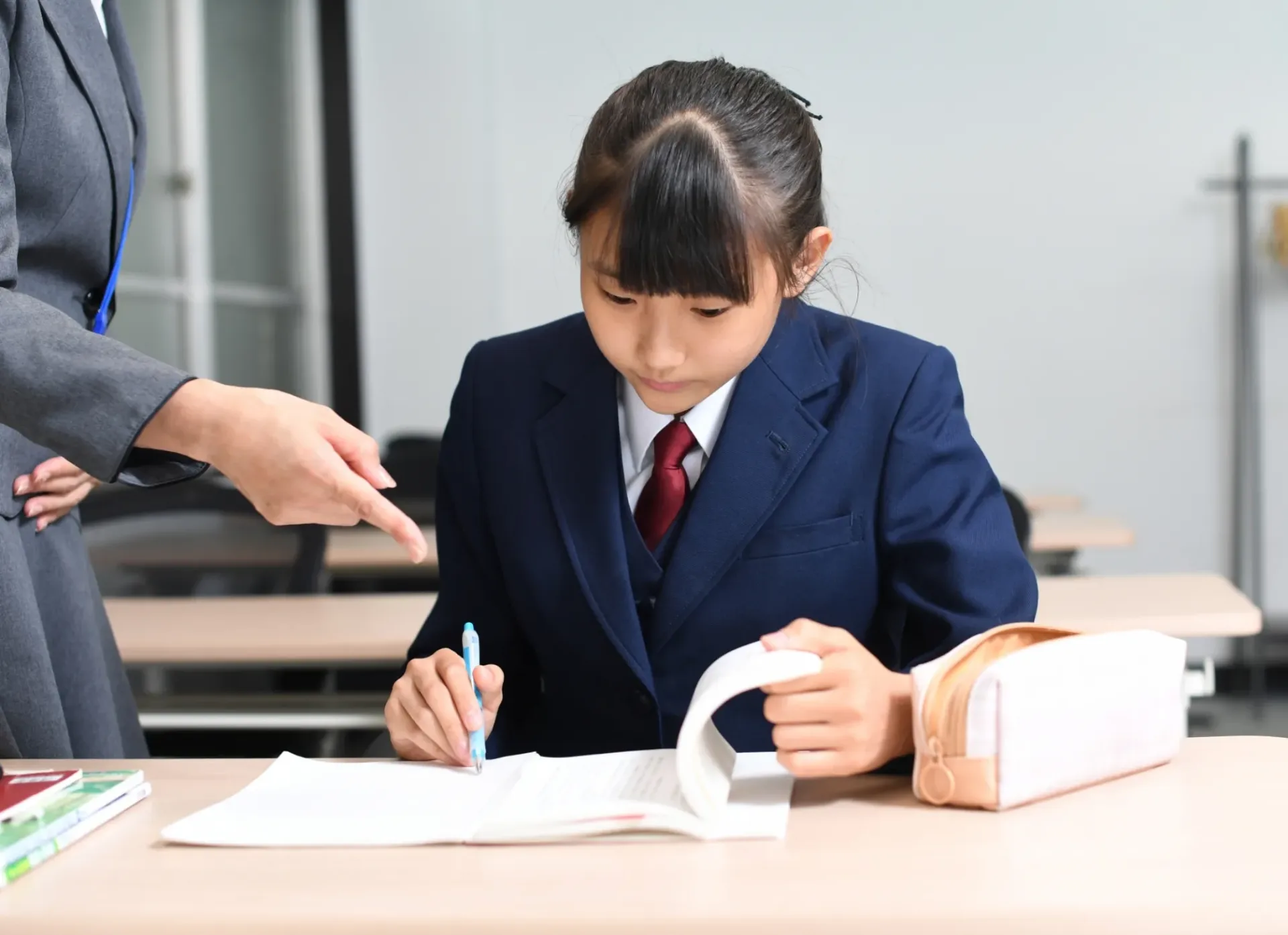 中学生が講師の指導を受けながら参考書に取り組んでいる様子